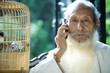 Photo: Elderly man wearing traditional Chinese clothing, using cell phone, next to bird cage Elderly man wearing traditional Chinese clothing, using cell phone, next to bird cage