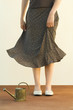 Woman standing beside watering can, holding skirt, cropped view