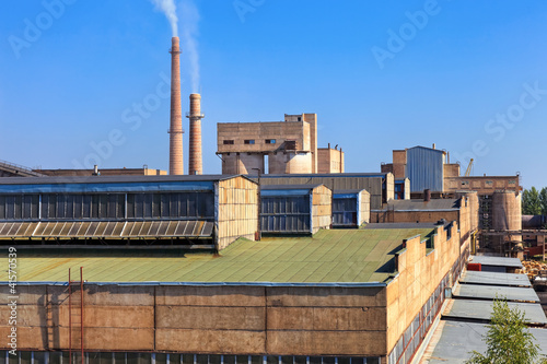 Foto: Large factory with smoking chimneys against the blue sky Large factory with smoking chimneys against the blue sky