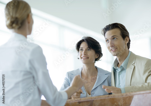 Photo: Couple at counter speaking to receptionist Couple at counter speaking to receptionist