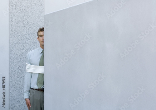 Photo: Businessman tied up, standing partially hidden behind wall Businessman tied up, standing partially hidden behind wall