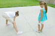 Girl drawing hopscotch game on driveway while second girl waits