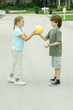 Girl handing boy ball in residential street
