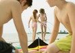 Boys preparing kite on beach, girls with hoola hoops in background