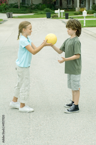 Photo: Girl handing boy ball in residential street Girl handing boy ball in residential street