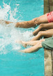 Man and children sitting on edge of swimming pool, splashing with legs