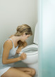 Young woman sitting on floor, leaning against toilet bowl