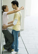 Teenage couple standing with arms around each other, leaning against wall