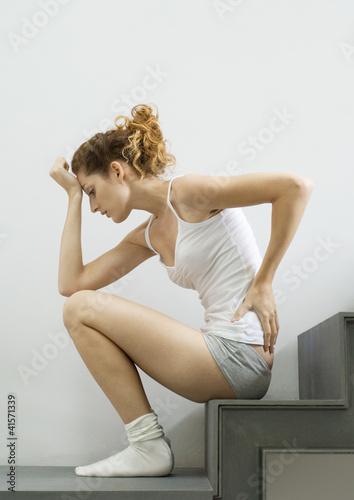 Photo: Young woman in tank top and underwear sitting on step, holding back Young woman in tank top and underwear sitting on step, holding back