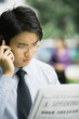 Businessman reading newspaper and using cell phone, frowning