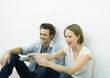 Photo: Teenage girl and young man sitting on floor, girl pointing remote control out of frame Teenage girl and young man sitting on floor, girl pointing remote control out of frame