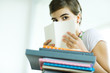 Teen girl with stack of homework, hiding face behind book, portrait