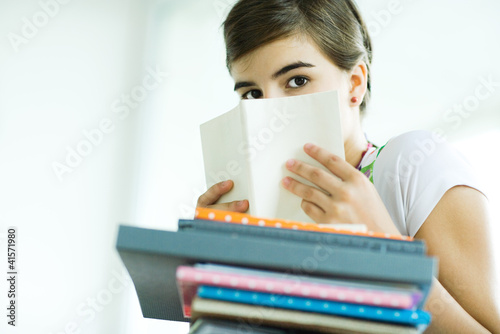 Photo: Teen girl with stack of homework, hiding face behind book, portrait Teen girl with stack of homework, hiding face behind book, portrait