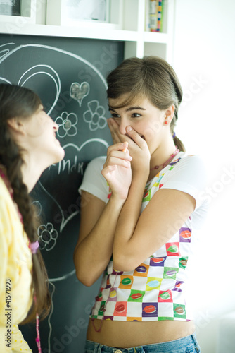 Foto: Young female friends writing names in hearts on chalkboard, laughing Young female friends writing names in hearts on chalkboard, laughing