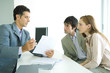 Young couple sitting across desk from businessman, businessman explaining document
