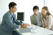 Young couple sitting across desk from businessman, businessman pointing to document