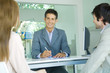 Young couple sitting across desk from smiling businessman, focus on businessman