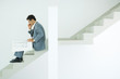Man in suit sitting on stairs, looking at blueprints, using cell phone