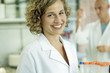 Female lab worker holding rack of empty test tubes, smiling at camera, portrait
