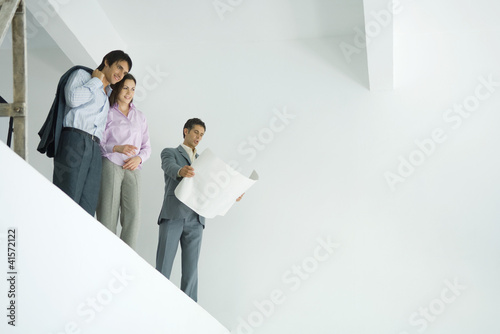 Photo: Young couple standing with architect, looking over unfinished interior, low angle view Young couple standing with architect, looking over unfinished interior, low angle view