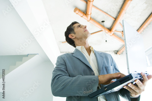 Photo: Well-dressed man using laptop, inspecting unfinished home interior Well-dressed man using laptop, inspecting unfinished home interior