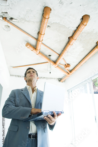 Foto: Well-dressed man using laptop, inspecting unfinished home interior Well-dressed man using laptop, inspecting unfinished home interior