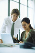 Photo: Male and female colleagues looking at laptop computer together, woman holding coffee cup Male and female colleagues looking at laptop computer together, woman holding coffee cup