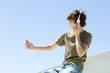 Photo: Teenage boy sitting outdoors, listening to headphones, looking at mp3 player, side view Teenage boy sitting outdoors, listening to headphones, looking at mp3 player, side view