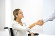 Woman in wheelchair shaking hands with businessman, cropped