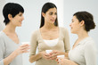 Three women chatting together, all holding disposable coffee cups