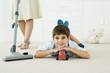 Photo: Little boy lying on the ground with toys, smiling at camera, mother vacuuming around him Little boy lying on the ground with toys, smiling at camera, mother vacuuming around him