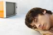 Young man resting head on arms, eyes closed, television in background