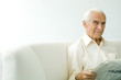 Senior man sitting on sofa, holding newspaper, smiling at camera