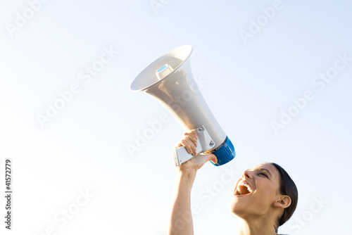 Photo: Woman shouting into megaphone, low angle view, cropped Woman shouting into megaphone, low angle view, cropped