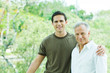 Young man with arm around his father's shoulder, both smiling at camera, portrait