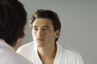 Man examining his face in the mirror, wearing bathrobe