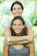 Photo: Mother standing behind teenage daughter, embracing her, both smiling at camera, portrait Mother standing behind teenage daughter, embracing her, both smiling at camera, portrait