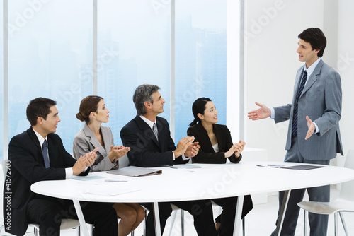 Photo: Business people applauding associate's presentation, sitting around table Business people applauding associate's presentation, sitting around table