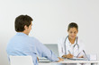 Female doctor sitting across from male patient at desk, writing down notes