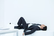 Businessman lying down on ledge in office