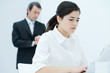 Young woman typing on laptop, boss checking time in background