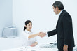 Professional woman sitting at desk, shaking hands with businessman
