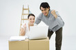 Photo: Young couple looking at laptop computer on top of cardboard box, smiling, clenching fists Young couple looking at laptop computer on top of cardboard box, smiling, clenching fists
