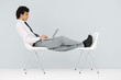 Businessman sitting in chair, feet up on another chair, using laptop
