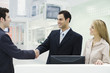 Photo: Three professionals standing at counter, men shaking hands Three professionals standing at counter, men shaking hands