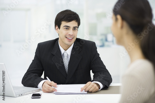 Photo: Businessman sitting at desk, talking with woman and smiling Businessman sitting at desk, talking with woman and smiling