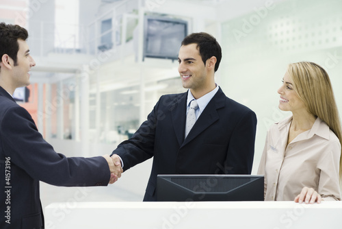 Photo: Three professionals standing at counter, men shaking hands Three professionals standing at counter, men shaking hands