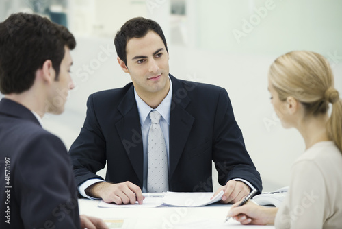 Photo: Businessman sitting with couple, woman signing document Businessman sitting with couple, woman signing document