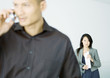 Businesswoman standing behind man talking on cell phone