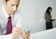 Foto: Businessman using electronic organizer and furrowing brow, woman standing in background Businessman using electronic organizer and furrowing brow, woman standing in background